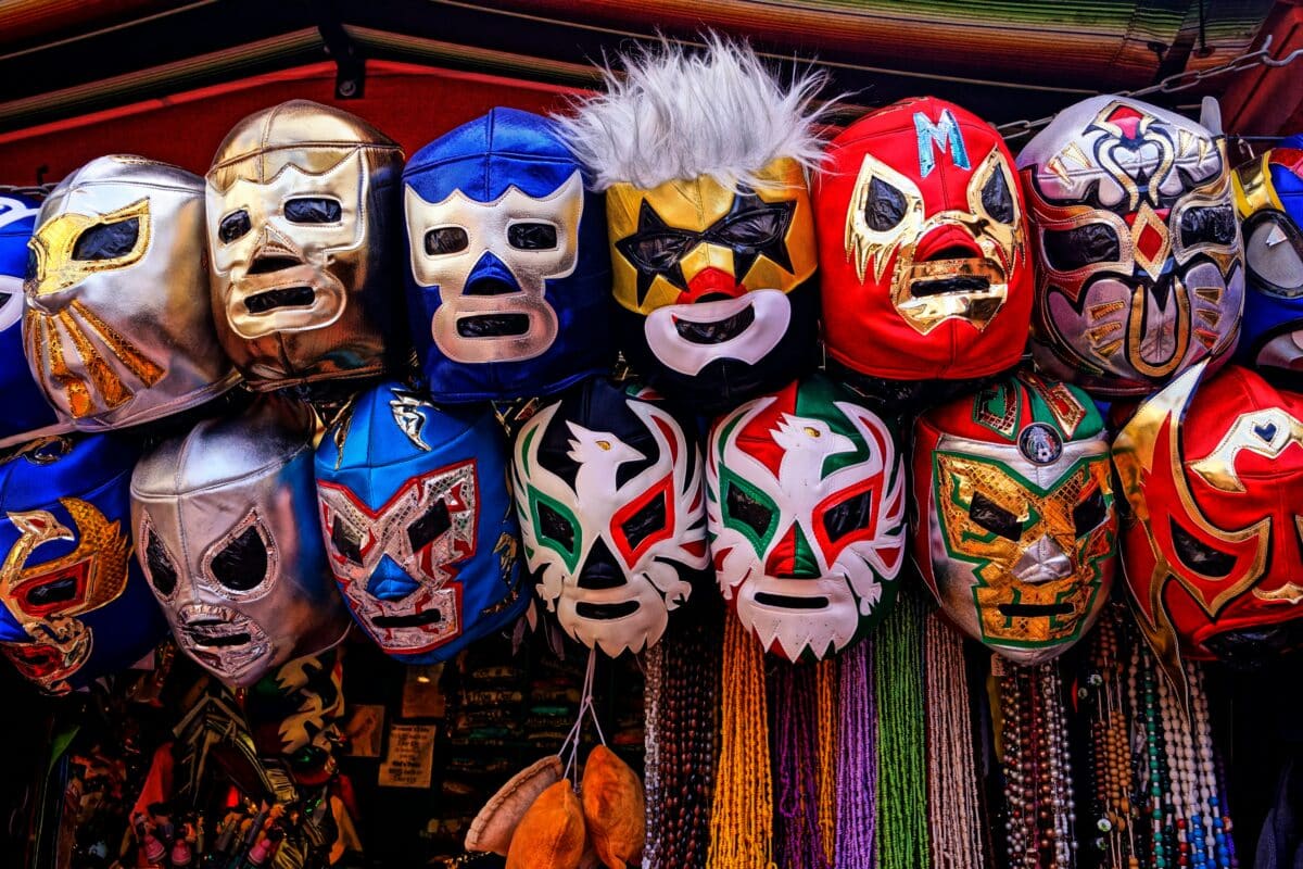 Esta imagem exibe uma coleção colorida de máscaras de lucha libre penduradas em um mercado. As máscaras, feitas de materiais brilhantes e decoradas com designs intricados e símbolos audaciosos, são típicas do wrestling profissional mexicano. Cada máscara representa diferentes personagens ou "luchadores", que são essenciais na cultura da lucha libre. Esta tradição de luta não só é um esporte emocionante, mas também uma forma de arte performática, onde as máscaras desempenham um papel crucial na criação de identidades heroicas ou vilanescas. As máscaras aqui capturadas variam em cores vibrantes e estilos, desde figuras animalescas a desenhos geométricos, cada uma com seu caráter único, refletindo a rica tradição e a paixão deste esporte.