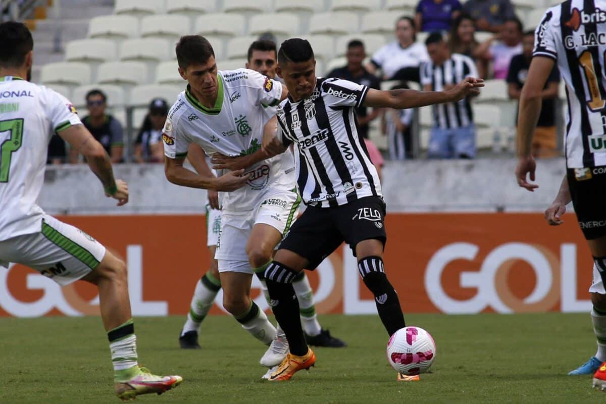 Jogador do ceará domina a bola entre dois marcadores do América mineiro e analisa melhor opção de passe.