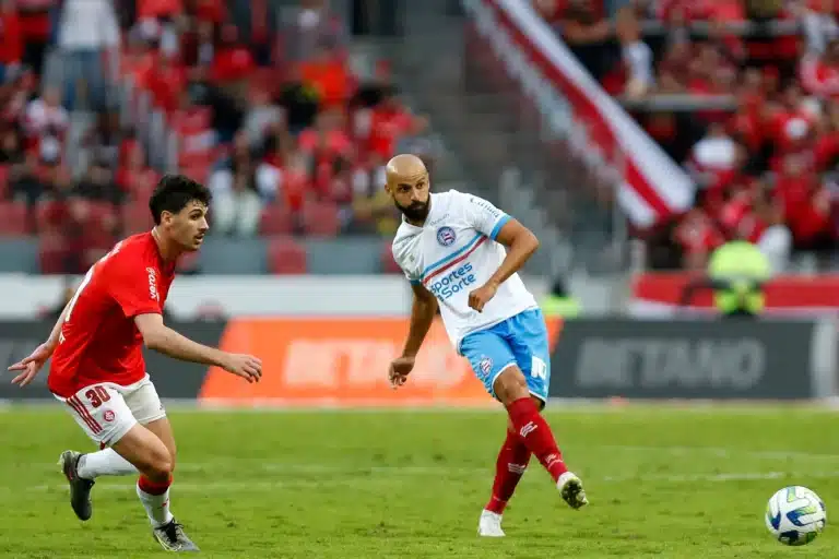 Jogador do Bahia Thacyano toca a bola enquanto marcador do Internacional observa.