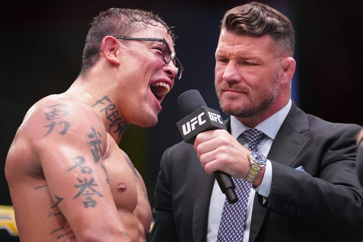 Um Caio Borralho sorridente, com óculos preto de nerd, é entrevistado por Michael Bisping após sua vitória sobre Cannonier ainda no octógono.