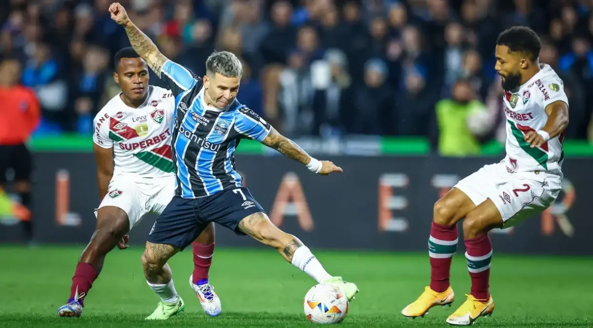 Jogador do Grêmio domina a bola entre os marcadores do Fluminense.
